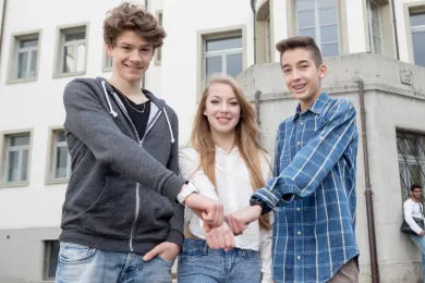 Drei Jugendliche stehen nebeneinander und lachen in die Kamera